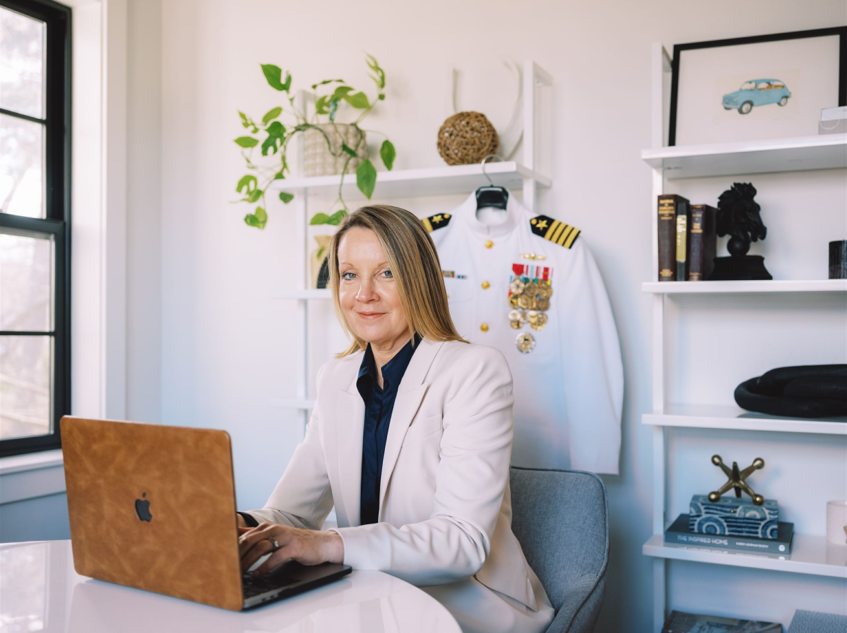 Woman in office with laptop and military uniform.